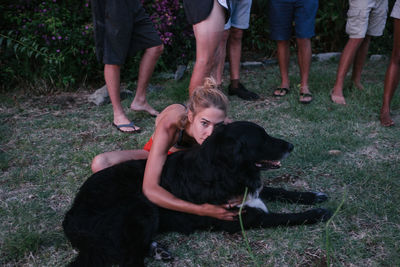 Portrait of woman embracing dog while sitting on grassy land