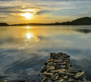 Stack of stones by lake against sky during sunset