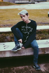 Full length portrait of young man sitting on wood