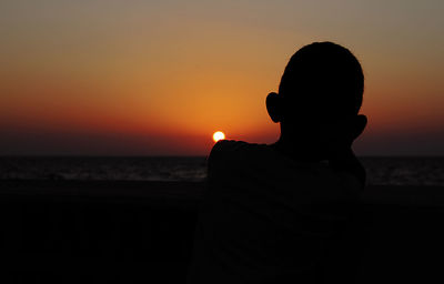 Silhouette boy standing at beach during sunset