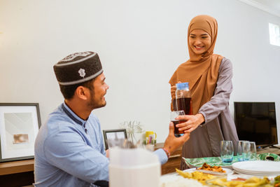 Smiling woman serving drink to guest at home