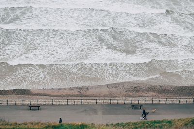 High angle view of people walking on footpath by surf at shore