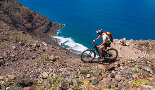 Man riding bicycle by cliff against sea