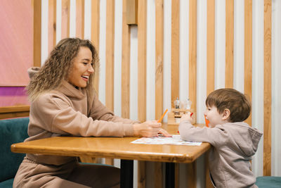 Young caucasian mother is sitting at a table in a cafe with her four-year-old son waiting