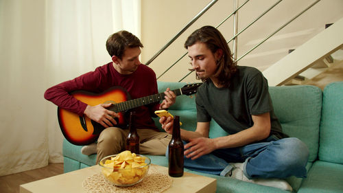 Homosexual couple playing guitar at home