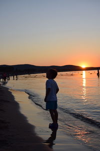 Rear view of boy on beach against sky during sunset