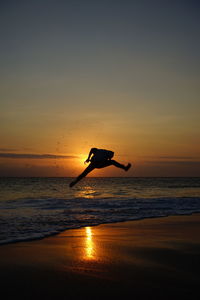 Silhouette person in sea against sky during sunset