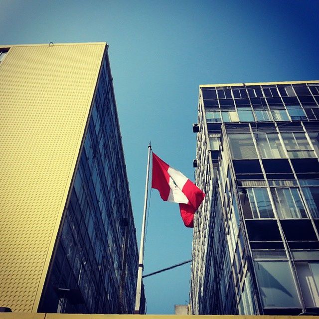 low angle view, building exterior, flag, patriotism, architecture, american flag, national flag, identity, built structure, clear sky, culture, city, modern, office building, skyscraper, red, striped, building, tall - high, day