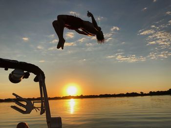 Full length of man diving into lake against sky during sunset