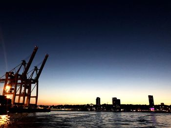 Cranes by sea against clear sky during sunset