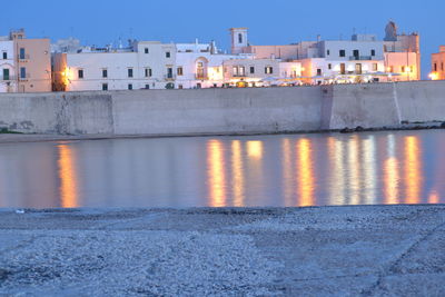 Canal by illuminated buildings in puglia at dusk