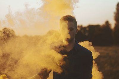 Portrait of young man standing amidst smoke outdoors
