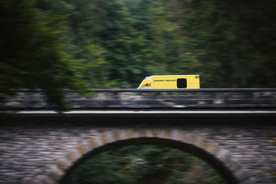 Ambulance car of emergency medical service in blurred motion on stone bridge in mountains. 
