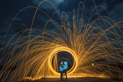 Couple holding umbrella while illuminated wire wool at night