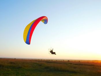 Man flying powered parachute over grassy field against clear sky during sunset