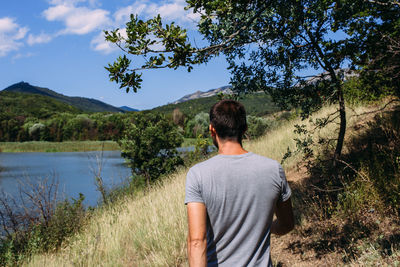 A young man is walking alone by the lake with a mountain landscape