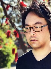 Portrait of young asian man in eyeglasses against flowering bottlebrush tree.
