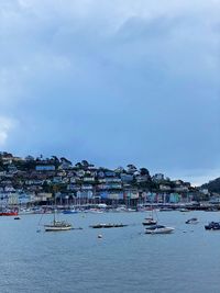 Sailboats moored in harbor by buildings against sky