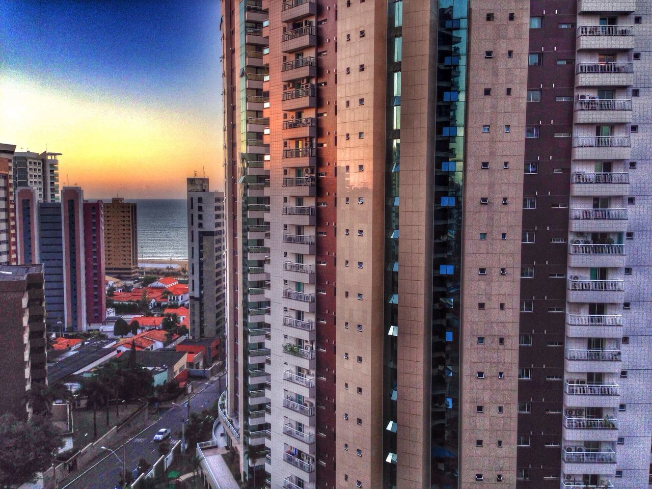 building exterior, architecture, city, built structure, cityscape, sunset, skyscraper, residential building, office building, modern, city life, residential structure, high angle view, sky, tall - high, building, car, residential district, orange color, tower
