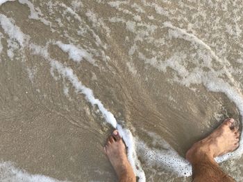 Low section of man standing on sandy beach