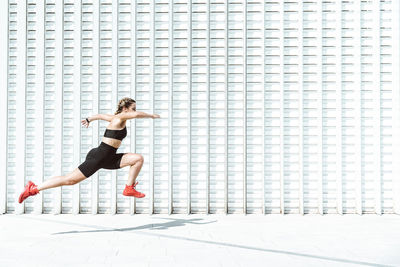 Young athlete jumping by white wall on sunny day