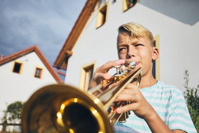 Low angle view of boy playing trumpet against house