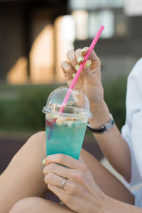 Refreshing non-alcoholic cocktail in a plastic cup with a straw in the hands of a woman