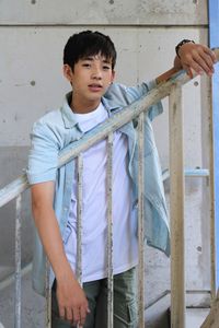 Portrait of boy holding metal railing against wall