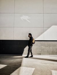 Side view of young man walking against shadow  patterned wall.