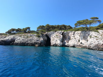 Rocks by sea against clear blue sky