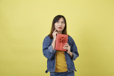 Portrait of young woman standing against yellow background