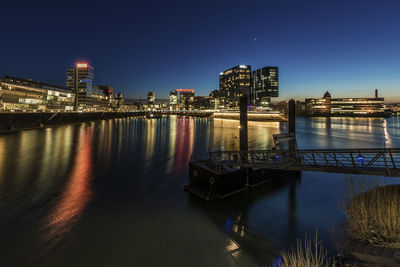 Illuminated buildings by river against sky at night