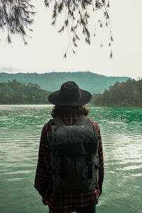 Rear view of man standing by lake against sky