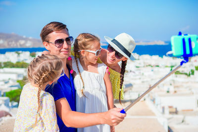 Happy family taking selfie from mobile phone with mykonos in background