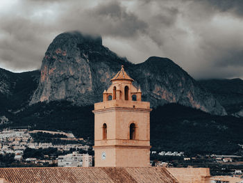 The town church tower in front of a mountain with clouds hovering above it