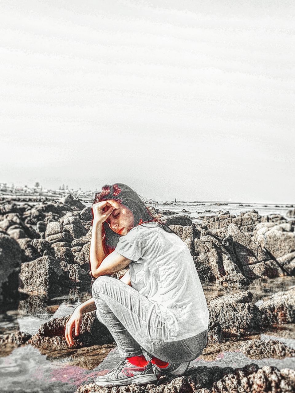 YOUNG WOMAN ON ROCKS AGAINST SKY