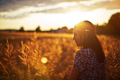 Young woman standing on wheat field against sky during sunset