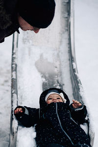 Father looking at baby girl playing on snow covered slide