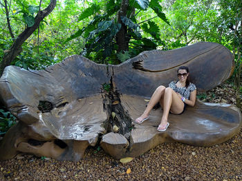 Full length of woman sitting on tree in forest