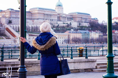 Rear view of woman standing by pole against buildings