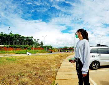 Woman standing by car against sky