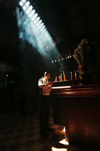 Full length of man burning candle while standing in temple