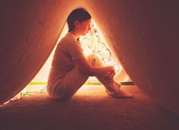 Side view of woman sitting under carpet at home