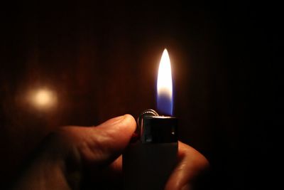 Cropped hand holding cigarette lighter in darkroom