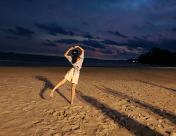 Rear view of girl standing on beach against sky during dusk