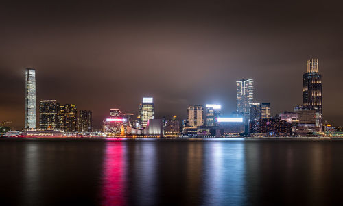 Illuminated buildings by river against sky at night