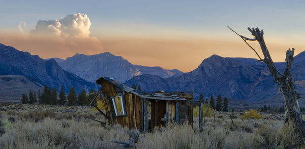 Smoke from the creek fire rises over the mountains at sunset with a weathered cabin 