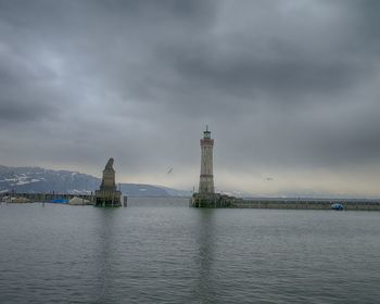 View of lighthouse in sea against cloudy sky