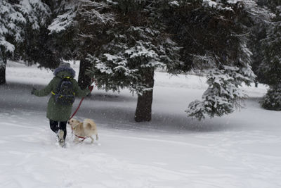 Rear view of girl playing with dog on snow covered field against trees