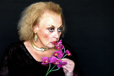 Senior woman smelling flower against black background